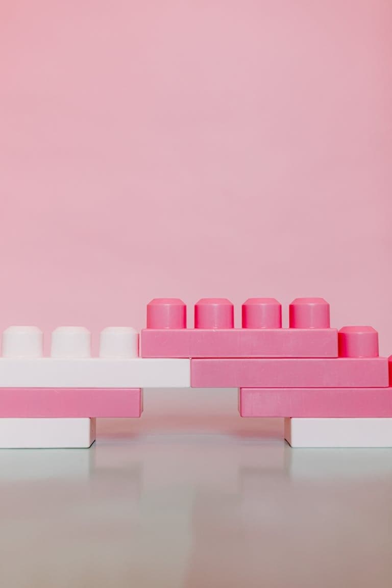 Pink and white toy building bricks stacked in a minimalist setup against a pink backdrop. Explore 5 unique value proposition examples for consultants and learn how to craft a UVP that sets your brand apart and attracts better-fit clients.